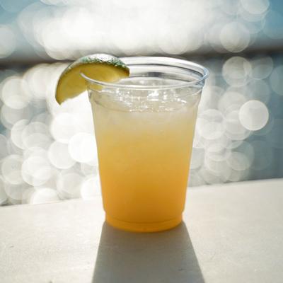Citrus-based cocktail served in a clear plastic cup with a lime wedge garnish.
