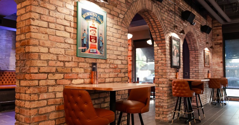 Interior, tables for two with bar chairs by a brick wall with openings