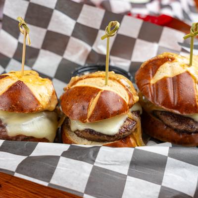 Three savory mini sliders with melted white cheese on toasted pretzel buns.