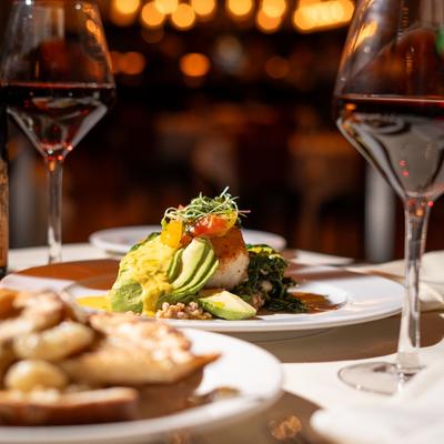 Seared scallop with avocado, grains, and greens, accompanied by two glasses of red wine.