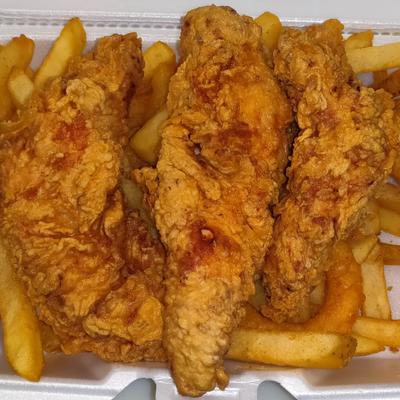 Fried chicken tenders rest on a bed of French fries in a takeout container.