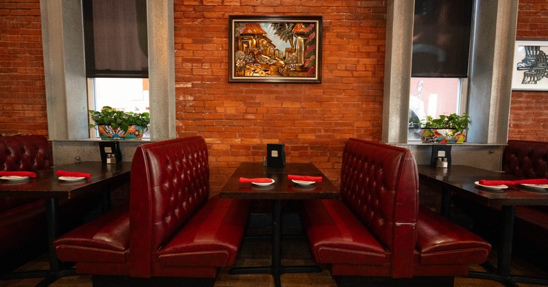 Interior, booth with red leather seating against a brick wall, framed by windows with plants