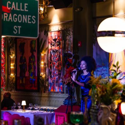 Singer performing on stage, with colorful artwork in the background.