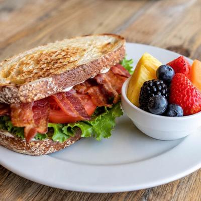 BLT sandwich served on a toasted bread with a side of fresh fruit.
