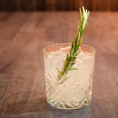 A cocktail served in a rocks glass, garnished with a sprig of rosemary.