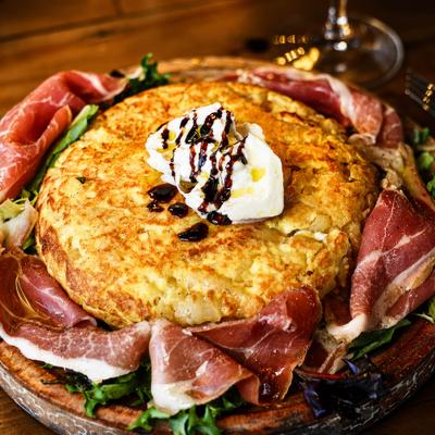 Spanish Tortilla topped with a dollop of cheese, surrounded by slices of prosciutto.
