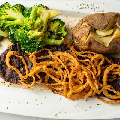 Grilled skirt steak with crispy onion strings, broccoli, and a baked potato.
