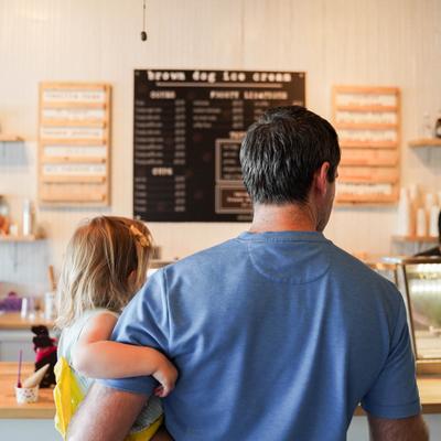 A man in a blue shirt holds a small girl in a yellow dress in an ice cream shop.