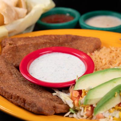Two breaded fish fillets, Mexican tartar sauce, rice, salad, and avocado slices.
