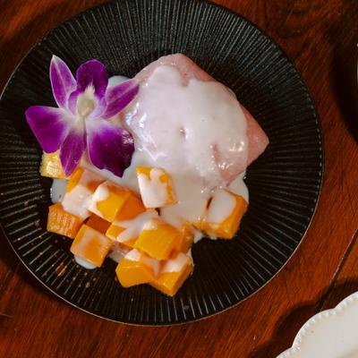 Thai mango sticky rice dessert topped with coconut sauce and an orchid.