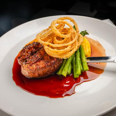Prime filet in red sauce accompanied by grilled asparagus spears and crispy onion rings.