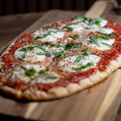 Margherita flatbread pizza with fresh basil on a wooden board.