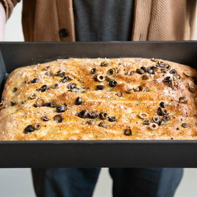 Freshly baked olive focaccia bread in a baking pan.