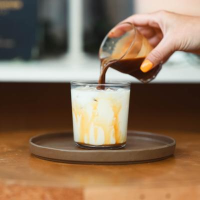 Hand pouring espresso over milk in a glass with ice.