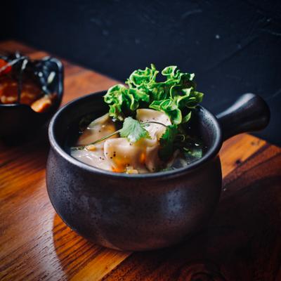 A dish of dumplings in a small, dark, ceramic pot, served on a wooden table.