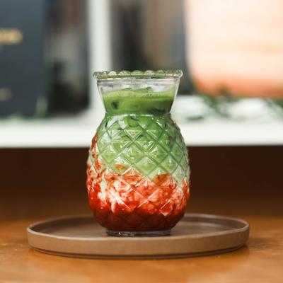 Strawberry Matcha Iced Latte served in a pineapple-shaped glass on a tray.