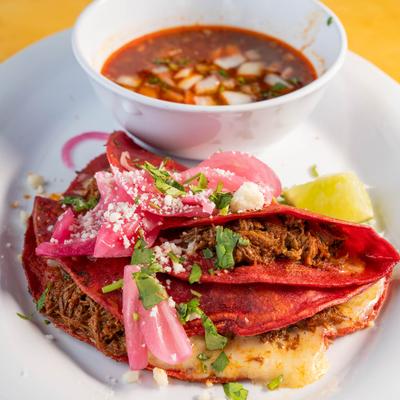 Birria tacos served on a plate with a small bowl of consommé.