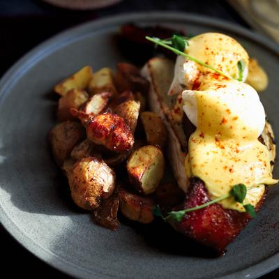 Eggs Benedict with hollandaise sauce, candied bacon, and roasted potatoes.