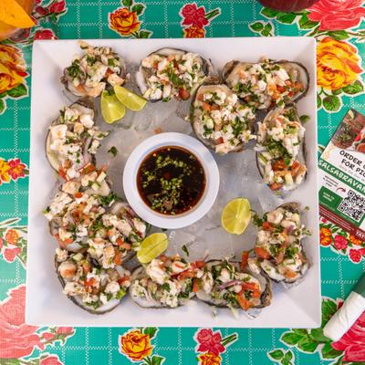 Ceviche-topped oysters served on a white square plate with a central dipping sauce.