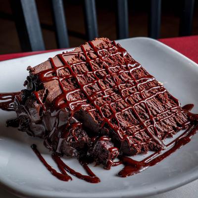 A slice of six layer chocolate cake, drizzled with chocolate sauce.