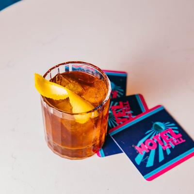 A glass of Old Fashioned on a white table with Motel No Tell coasters.