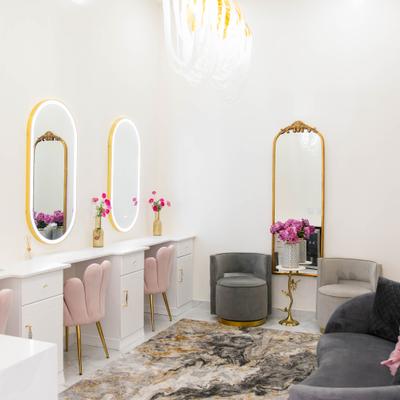 Room with multiple lighted mirrors, styling chairs and a seating area.