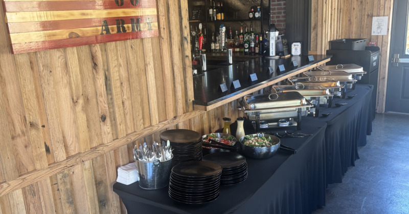 Buffet setup with chafing dishes, stacks of black plates, and silverware