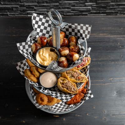 Multi-tiered appetizer tower featuring pretzel bites, sliders, onion rings fries and dips.