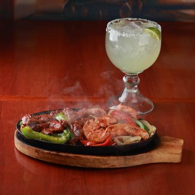 Sizzling Mixed fajita plate emitting steam, accompanied with a Margarita cocktail