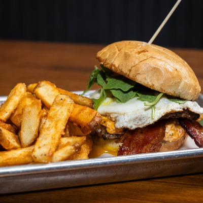 Bacon burger topped with a fried egg and greens, accompanied by thick-cut fries.
