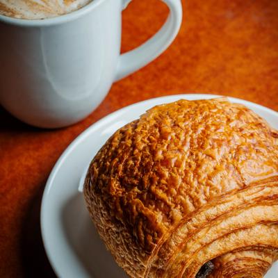 Croissant served on white plate alongside a cup of coffee.