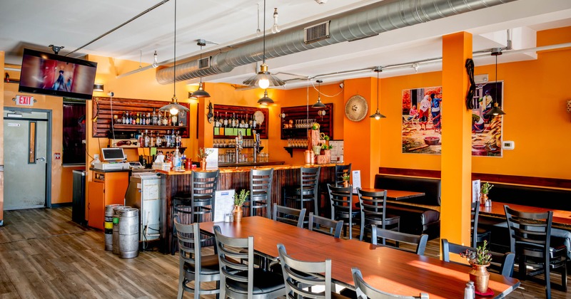 A bright orange-walled restaurant interior with wooden tables and a bar area