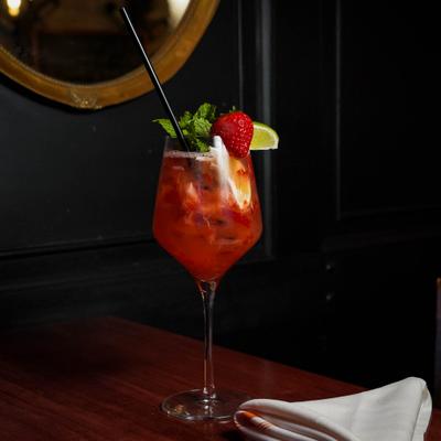 Cocktail in a wine glass, garnished with strawerry, mint and a lime wedge.