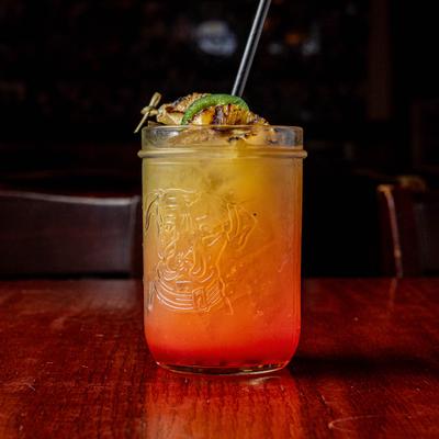 Yellow and red gradient cocktail in a mason jar garnished with grilled pineapple and jalapeno.