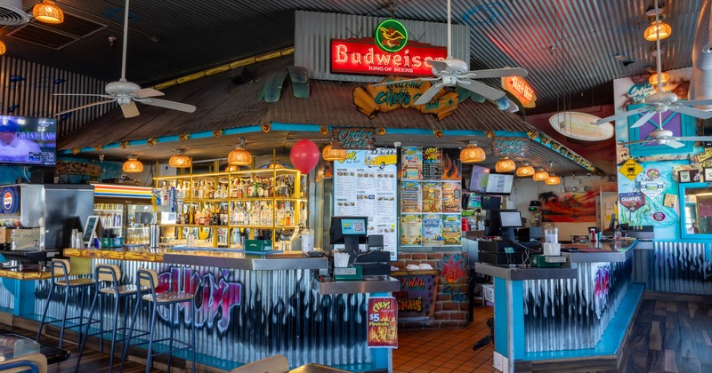 Indoor restaurant bar - tropical decor, graffiti artwork and a stocked shelf of beverages.