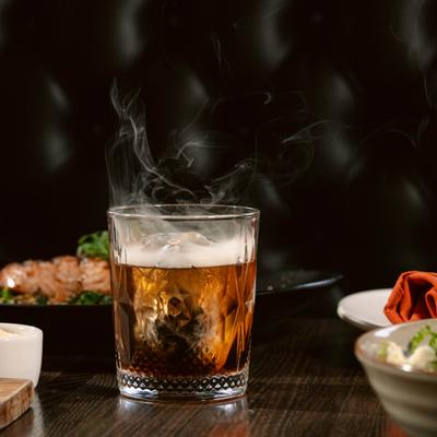 Smoked Old Fashioned served on a table with food.