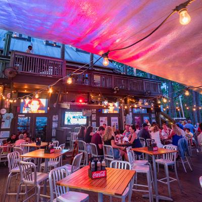 Ourdoor patio with table seating, string lights and multiple television screens.