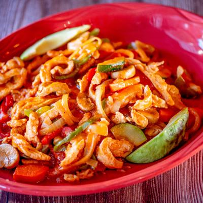 Chicken strips in red sauce with vegetables in red bowl.
