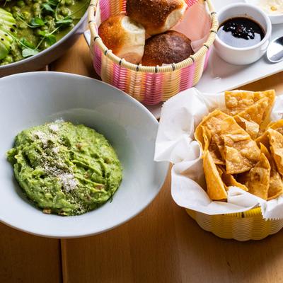 Guacamole with tortilla chips, bread rolls, and sauce on a table.