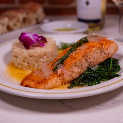 Seared salmon served with risotto and spinach, garnished with a purple orchid.