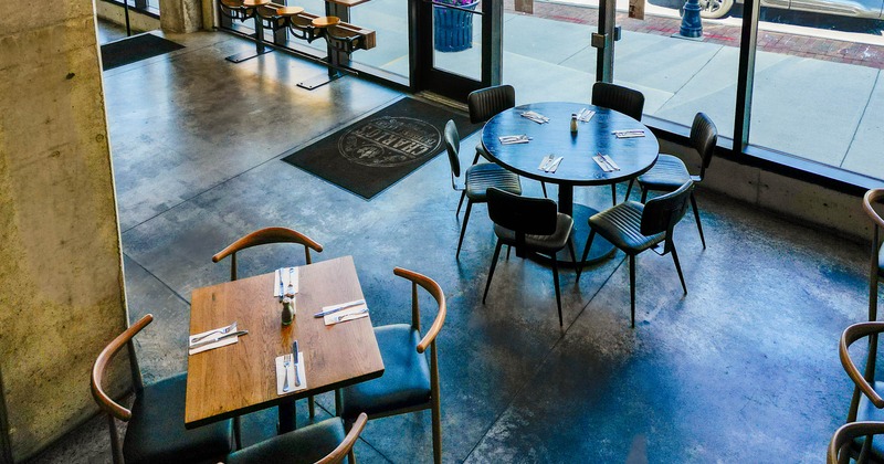 Dining area with two set tables, one square and one round, near large glass windows