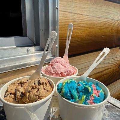 Single scoops of superman, espresso, and strawberry ice cream in to go cups with spoons..