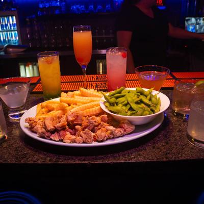 Fried chicken bites, fries, edamame, and assorted cocktails on a bar counter.