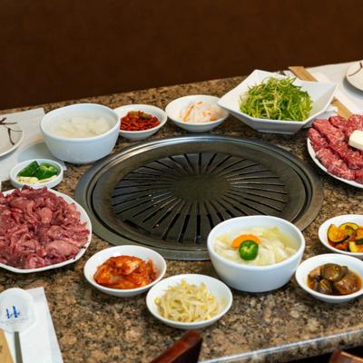 Korean BBQ setup with a central tabletop grill surrounded by meat and side dishes.