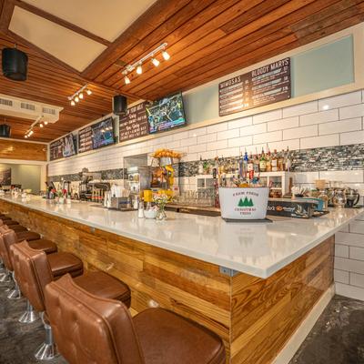 Bar area with brown leather stools, overhead menu boards, and shelves of liquor