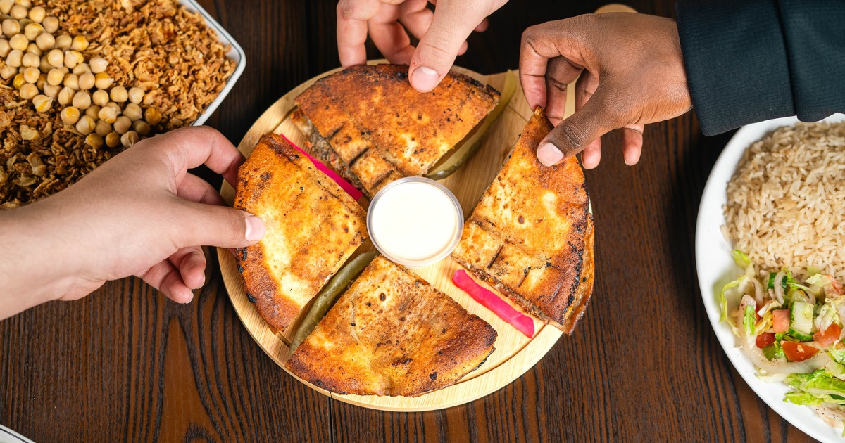 People sharing sliced stuffed flatbread around a dipping sauce