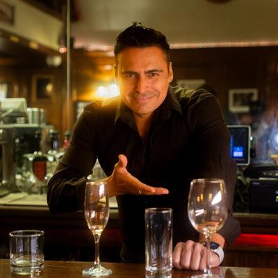 A bartender gestures toward glassware on a dimly lit counter.