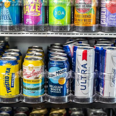 Various cans of beer on refrigerated shelves.