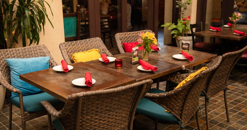 Dining table with red napkins and white plates, surrounded by wicker chairs with colorful cushions