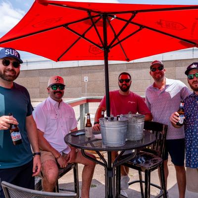 A group of friends enjoying cold beers under a red umbrella.
